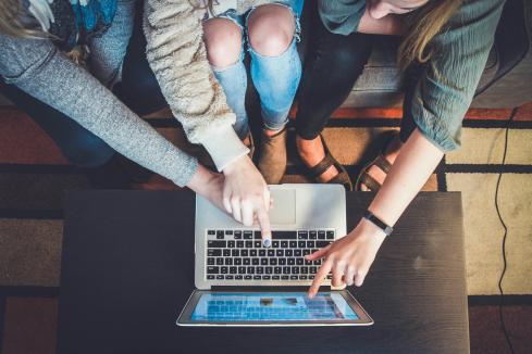 bird's eye view of a group of young people sitting on a bench, looking at a laptop together