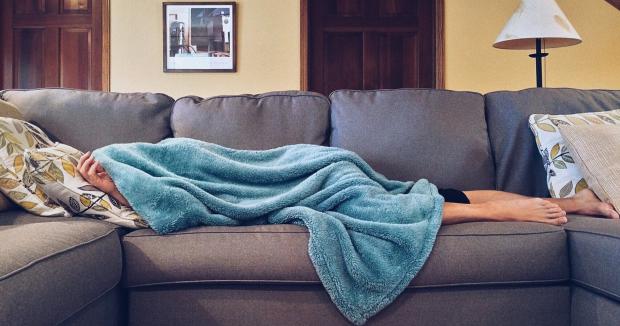 woman hiding under a blue blanket while lying on a couch