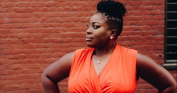 black woman in an orange top looking confident with her hands on her hips