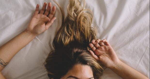 blonde woman lying in bed with her hands above her head