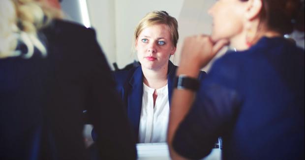 blonde woman sitting and facing two other women at a table having a discussion