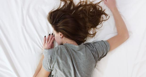bird's eye view of a woman with brown hair and a gray t-shirt lying face down on a bed