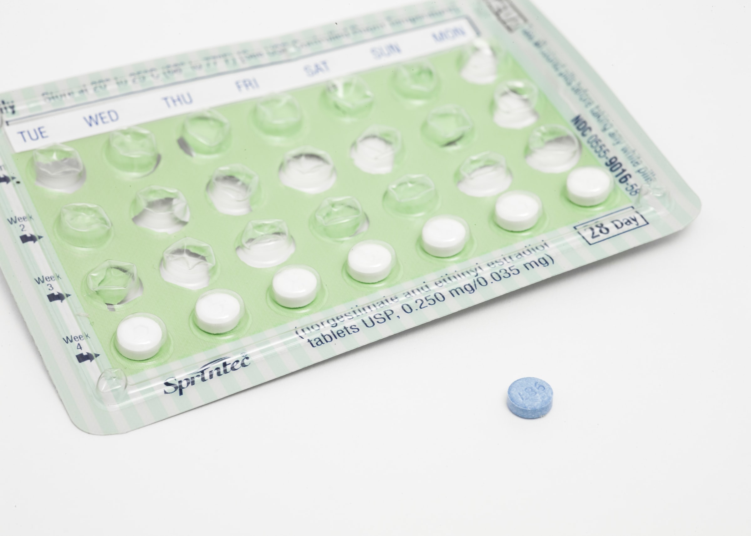 a blue tablet next to a monthly pack of oral contraceptives that is 3/4 empty