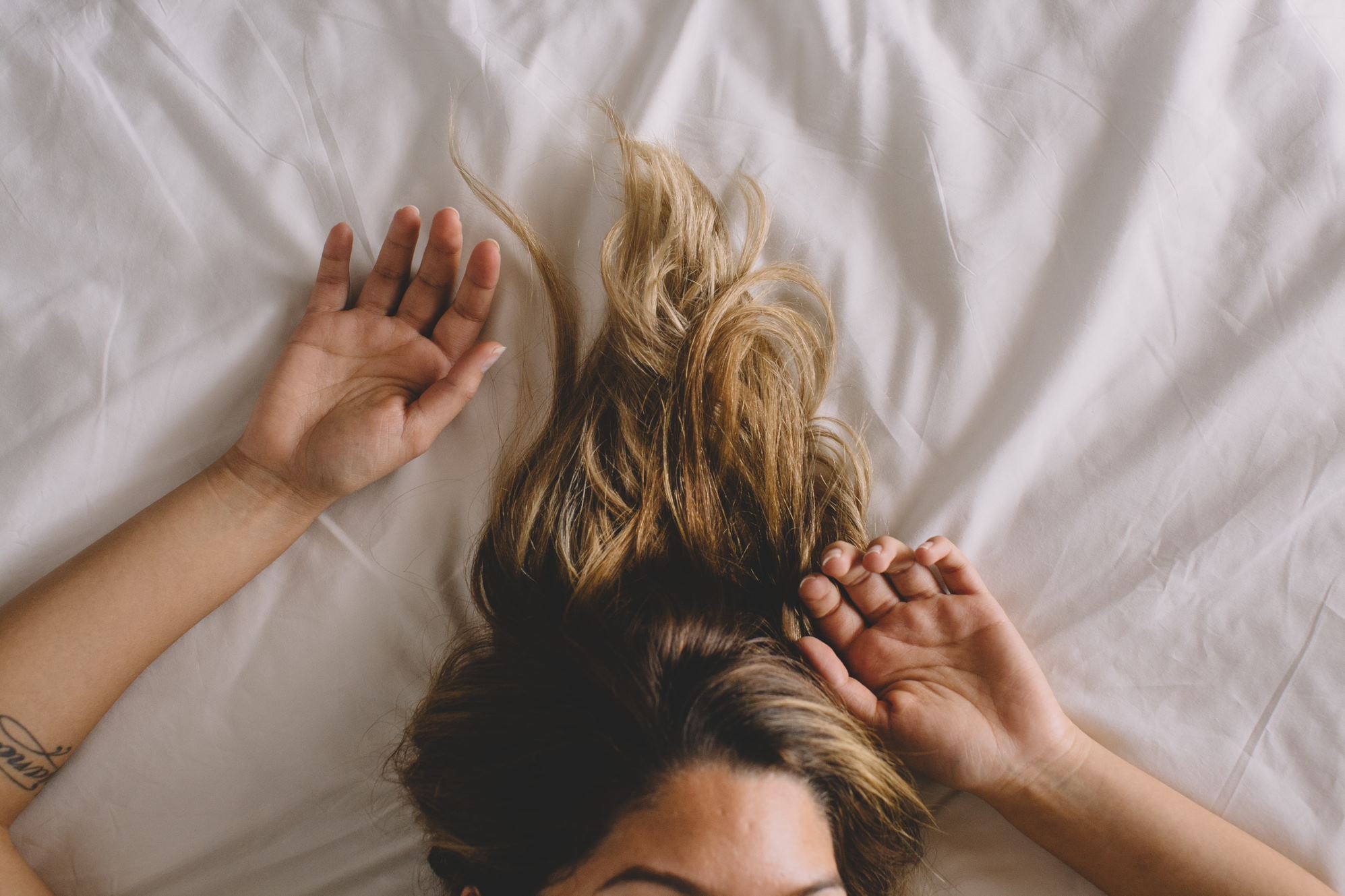 blonde woman lying in bed with her hands above her head