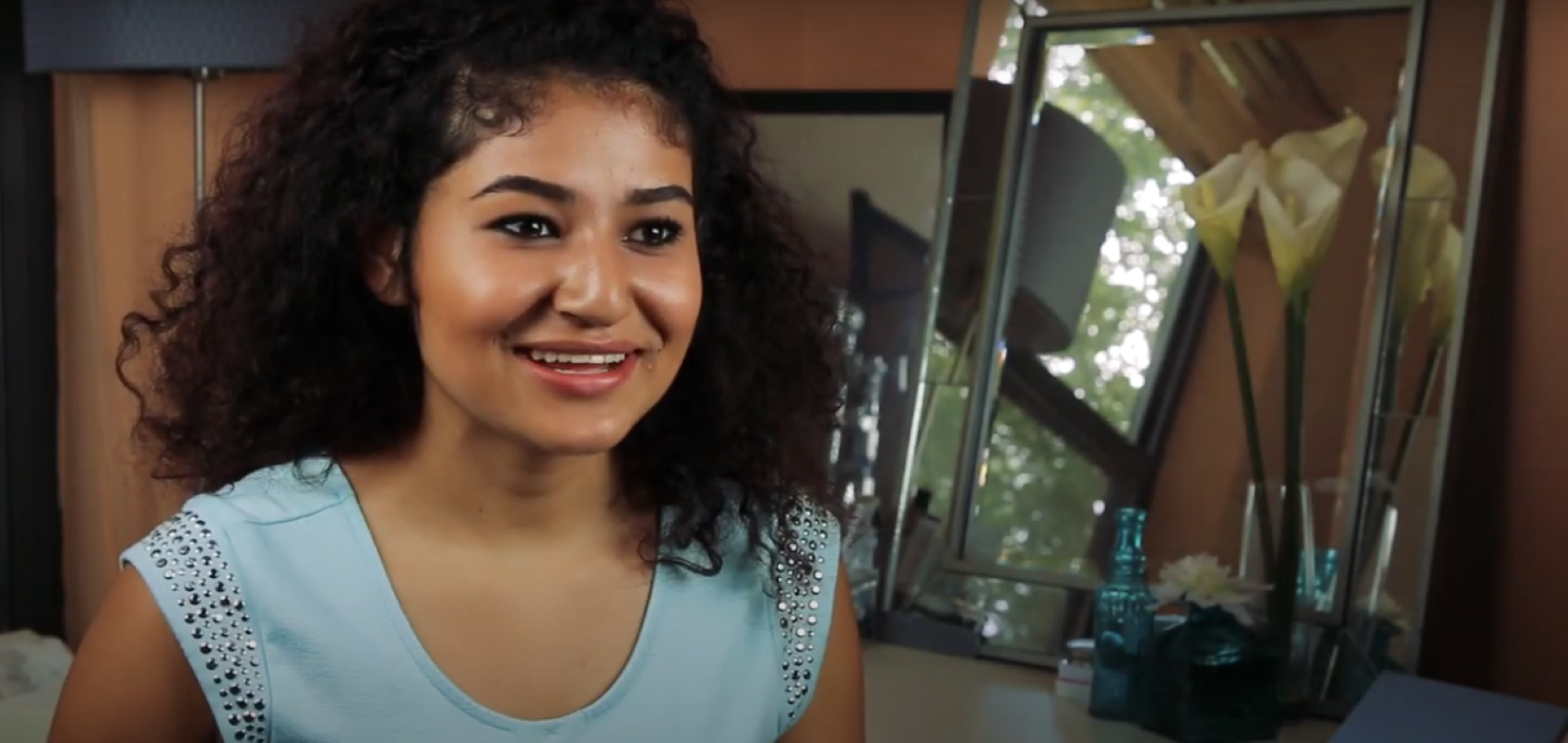 BIPOC woman with dark curly hair and a blue shirt talking about her birth control to camera