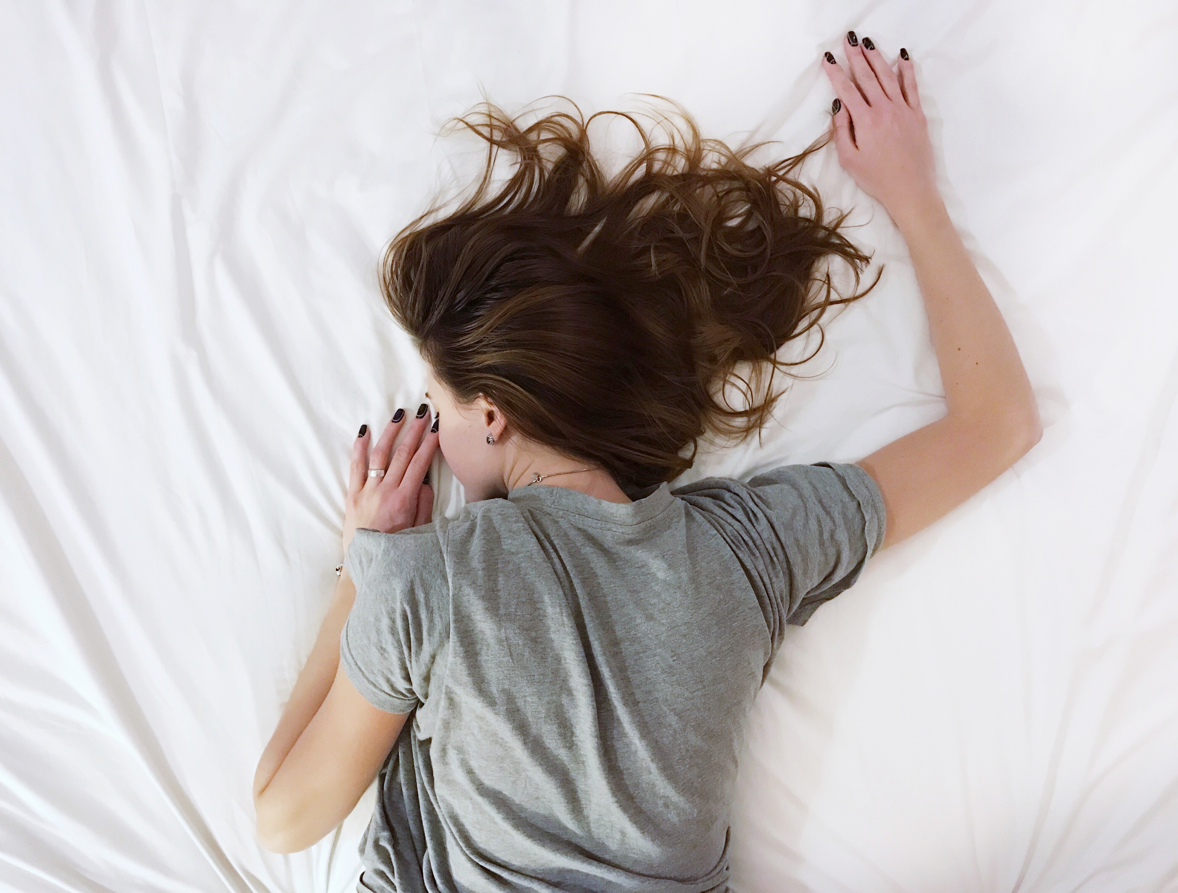 bird's eye view of a woman with brown hair and a gray t-shirt lying face down on a bed